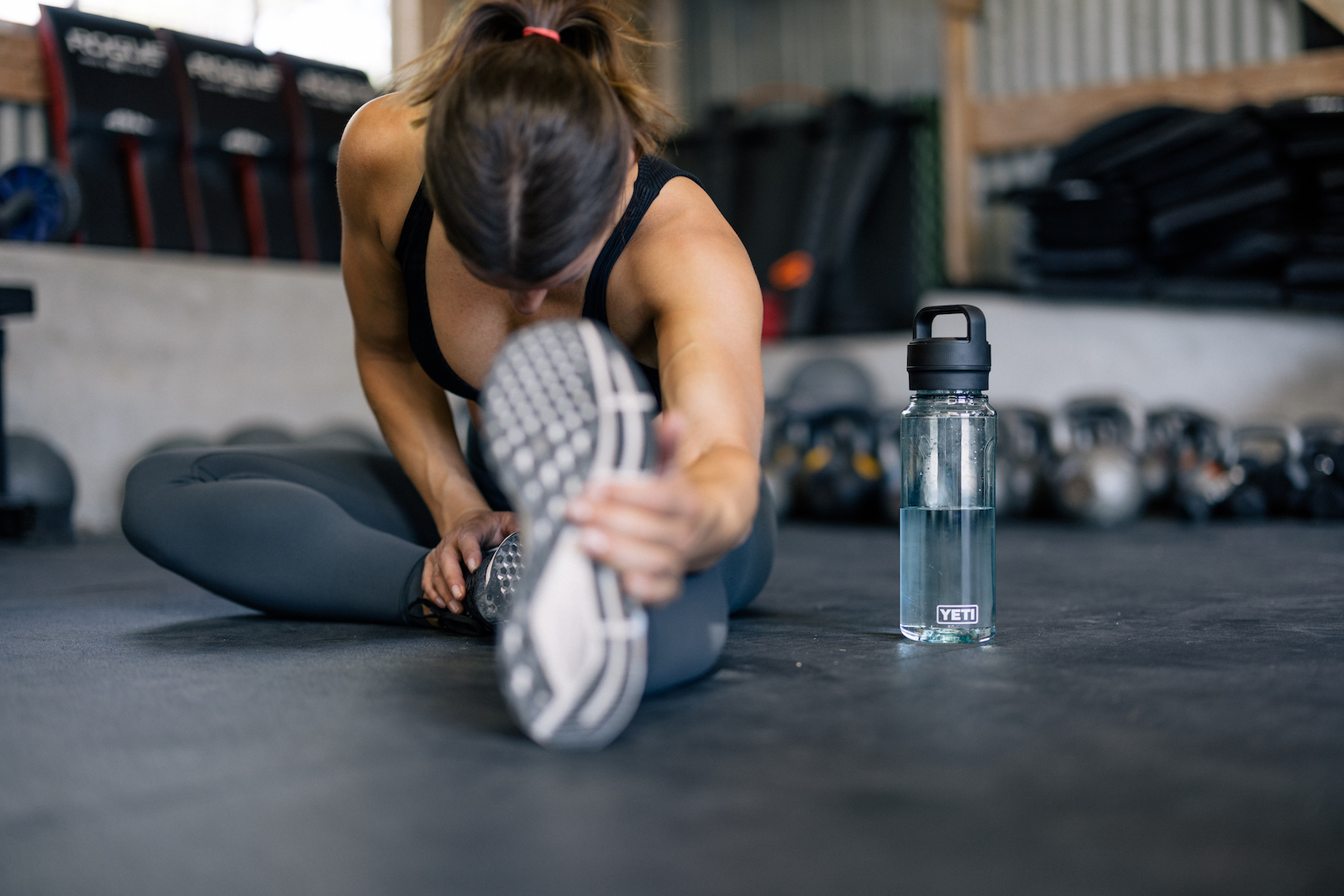 Woman stretching in gym with water bottle beside her