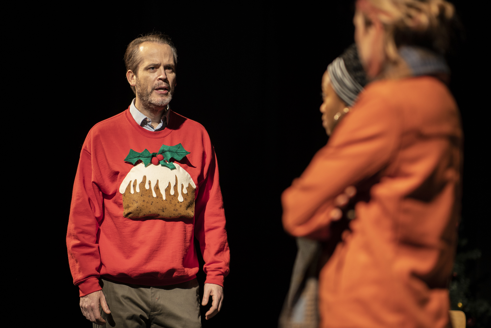 Man in a Christmas sweater talking to two women