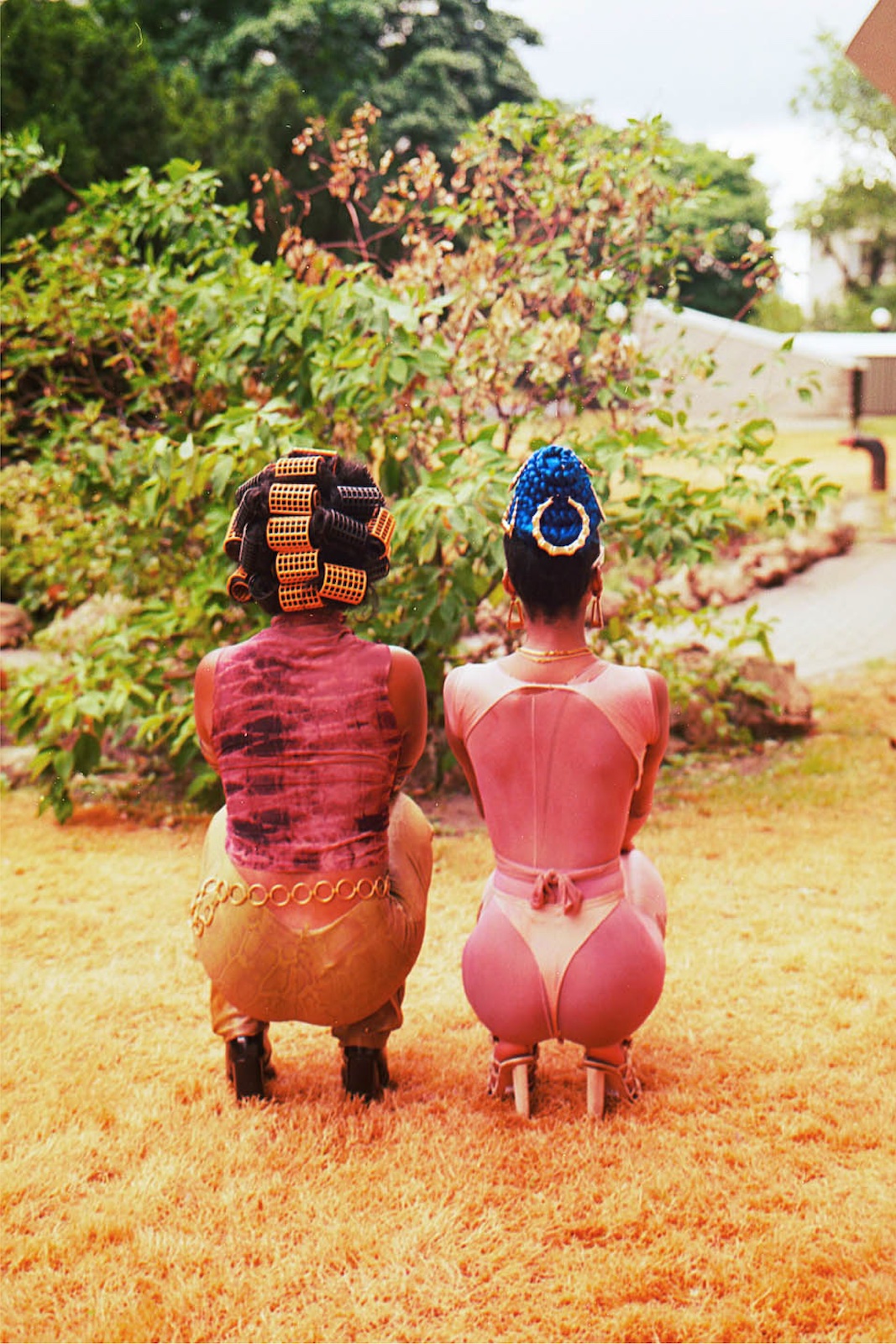 Two women squatting in yard, shown from behind