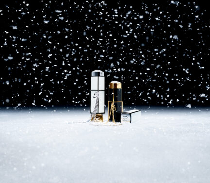 Two bottles of Chanel perfume set against a black background amid falling snow.