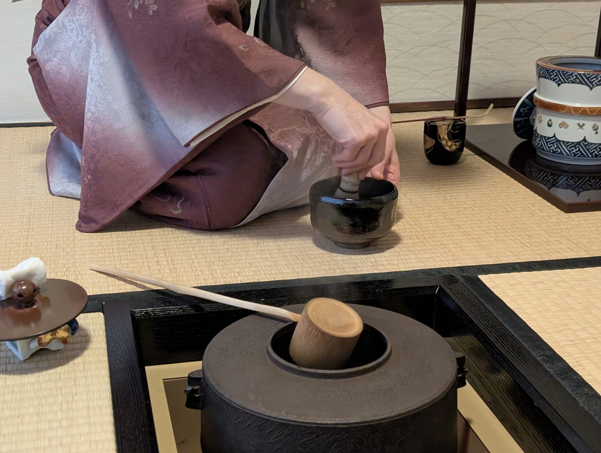 A woman whisks tea in front of a hearth.