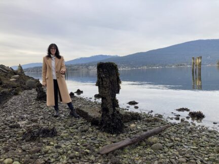 A young woman, Ranah Chavoshi, stands on the beach surrounded by seaweed used for compostable plastic.