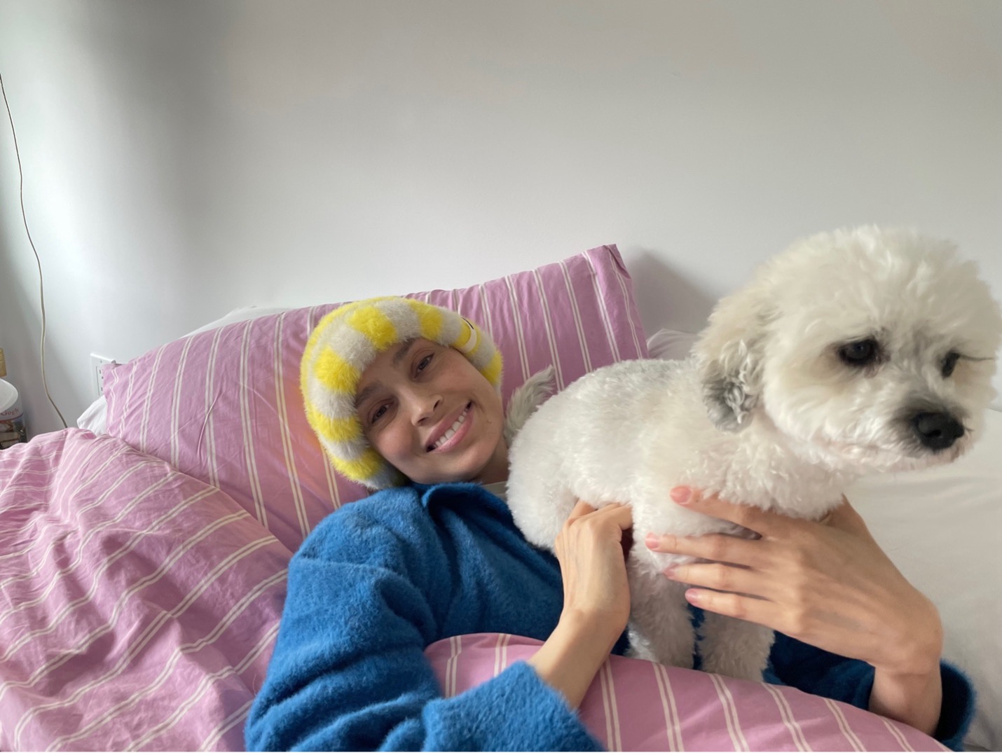 Hailey Merkt lies in a bed holding a small white dog.