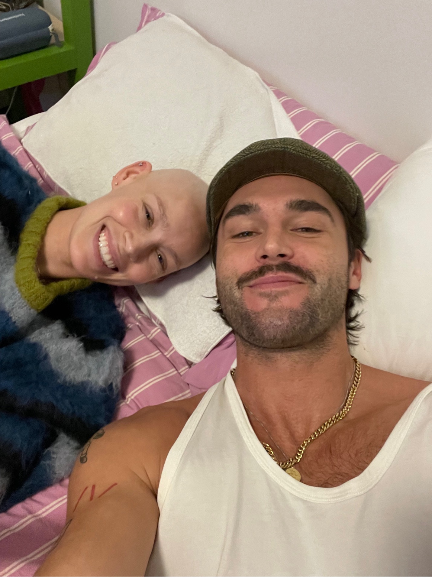 A young man and woman lie back on a bed smiling at the camera.