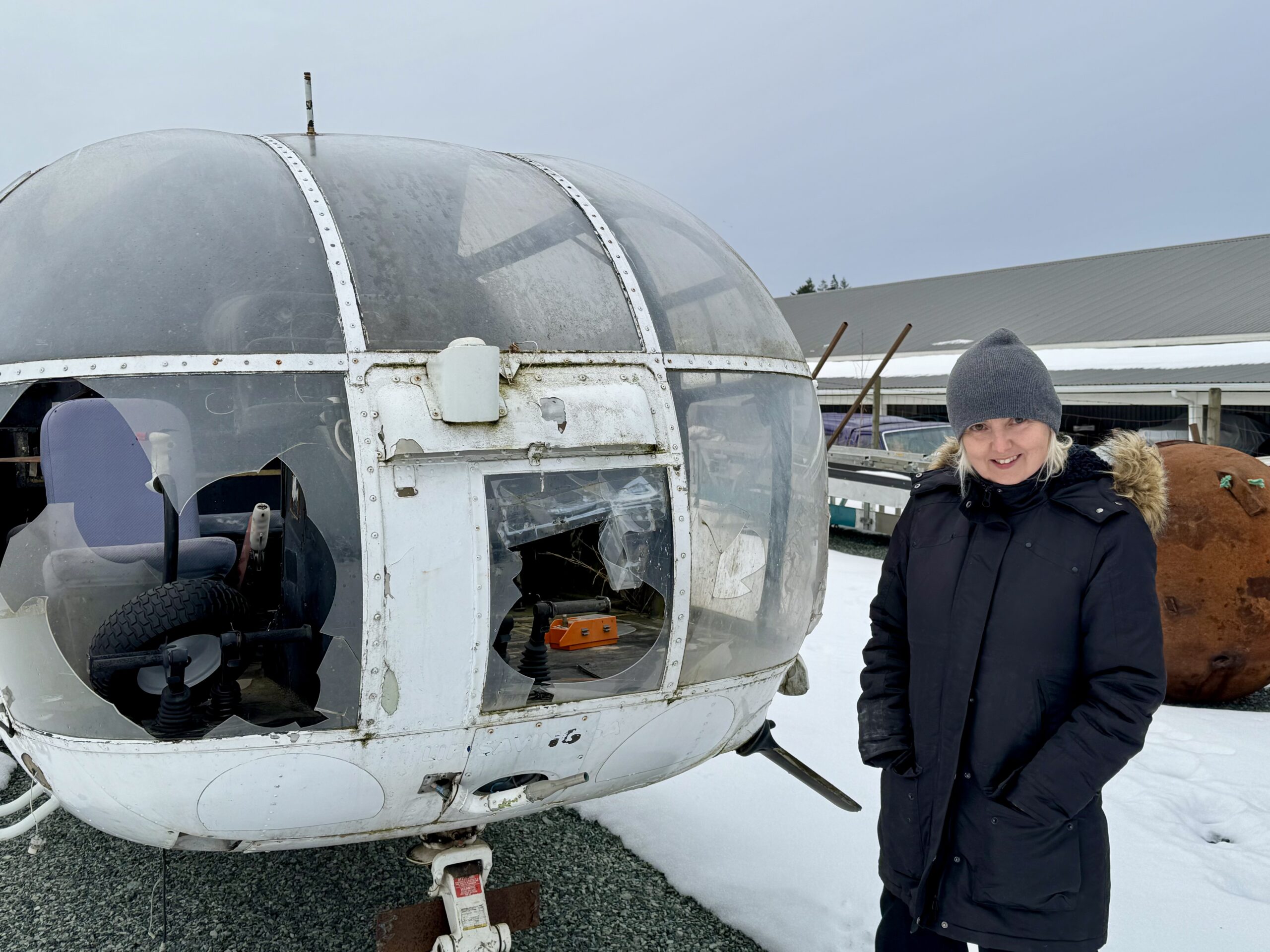 Ani Kyd Wolf stands next to a prop helicopter outdoors in winter.