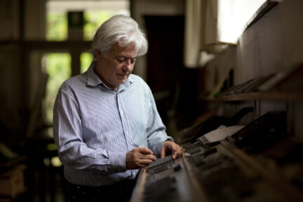 A man, Enrico Tallone, handles typesetting tools.