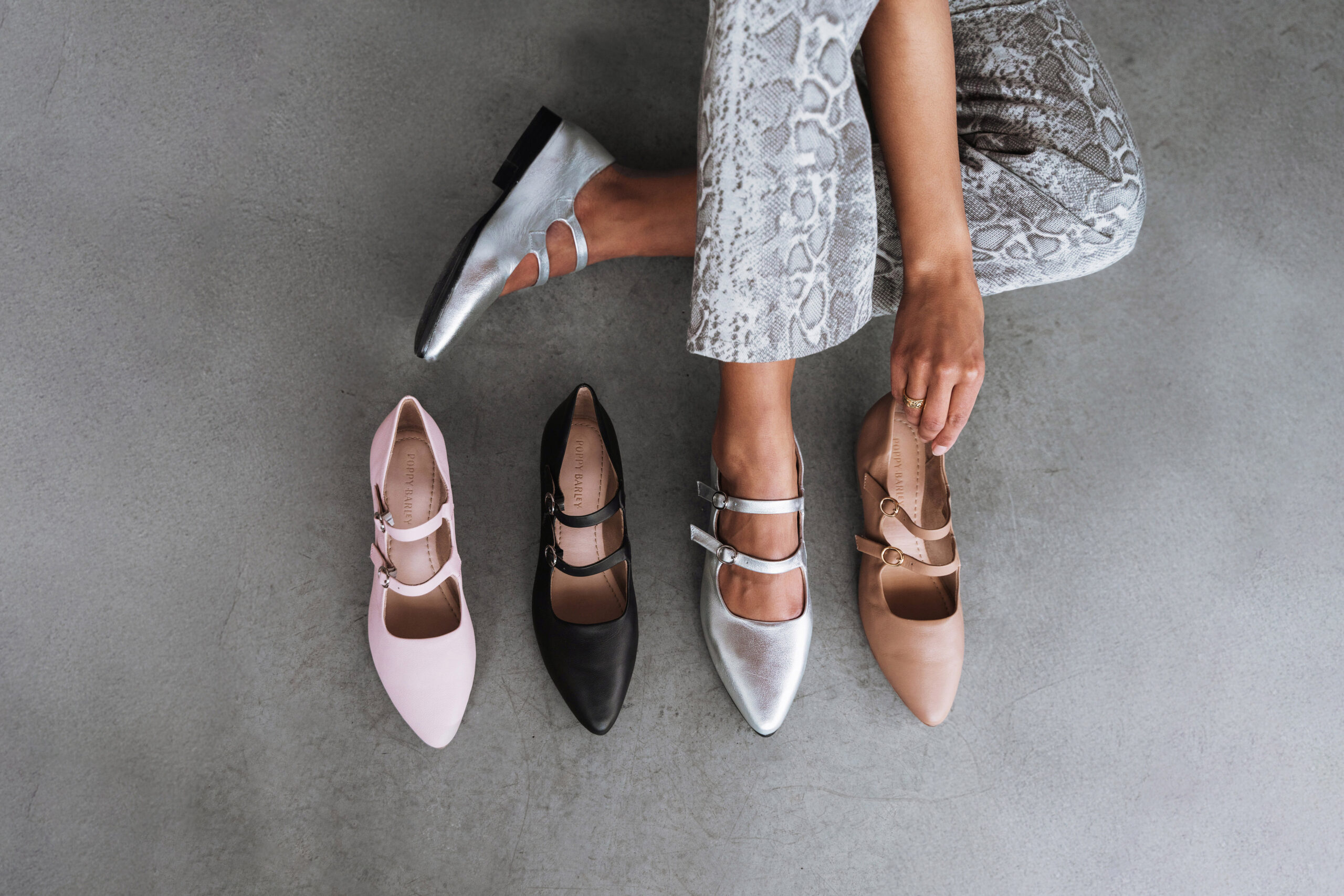 A woman's legs with four pairs of shoes.