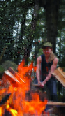 A woman chops wood in front of a fire
