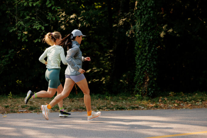 Two women in activewear and Hettas sneakers run together outdoors.