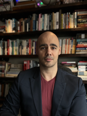 A headshot of a man, Miguel Eichelberger, in front of a bookcase.