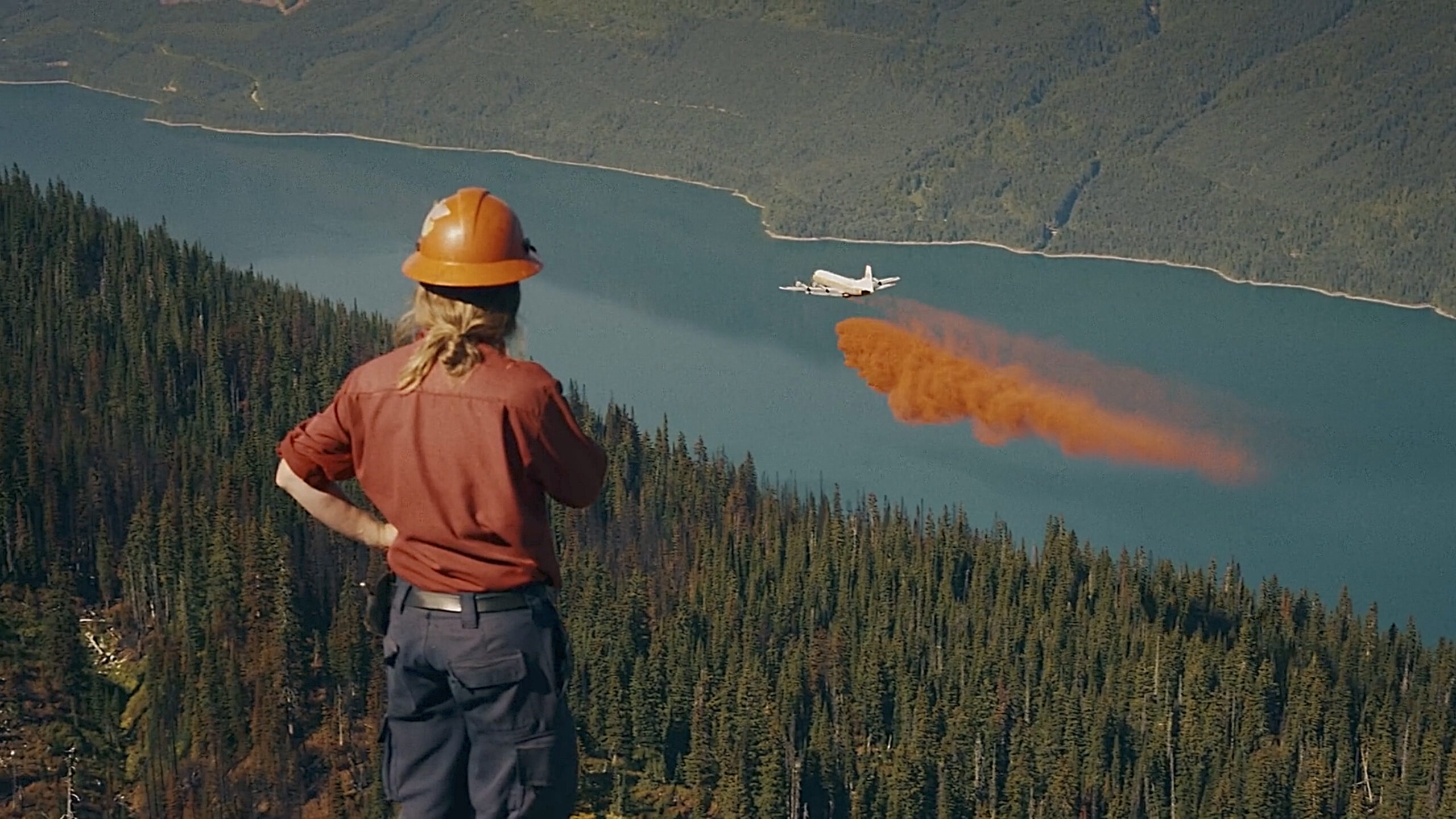 A firefighter surveys as a plane drops fire retardant on a forest.