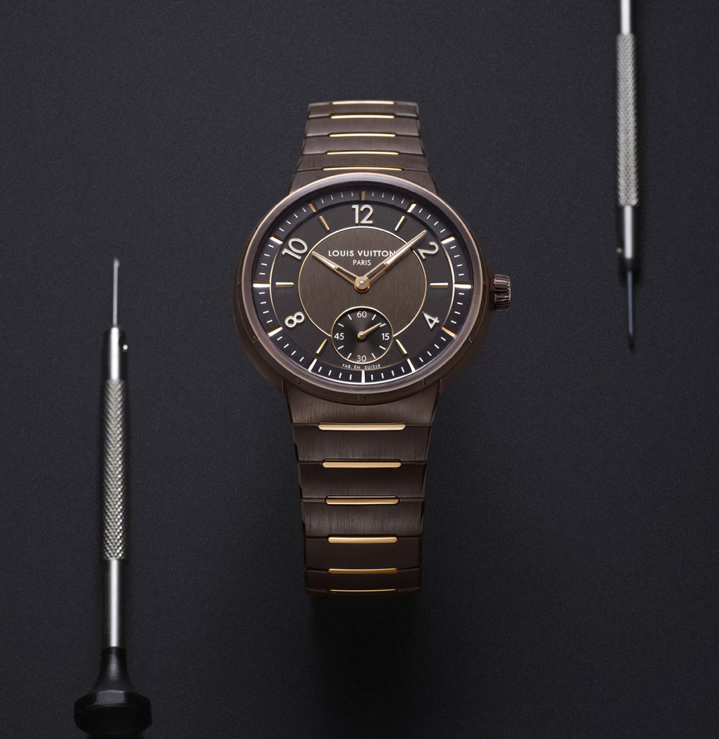 A brown watch from Louis Vuitton flanked by small watch adjusting tools.
