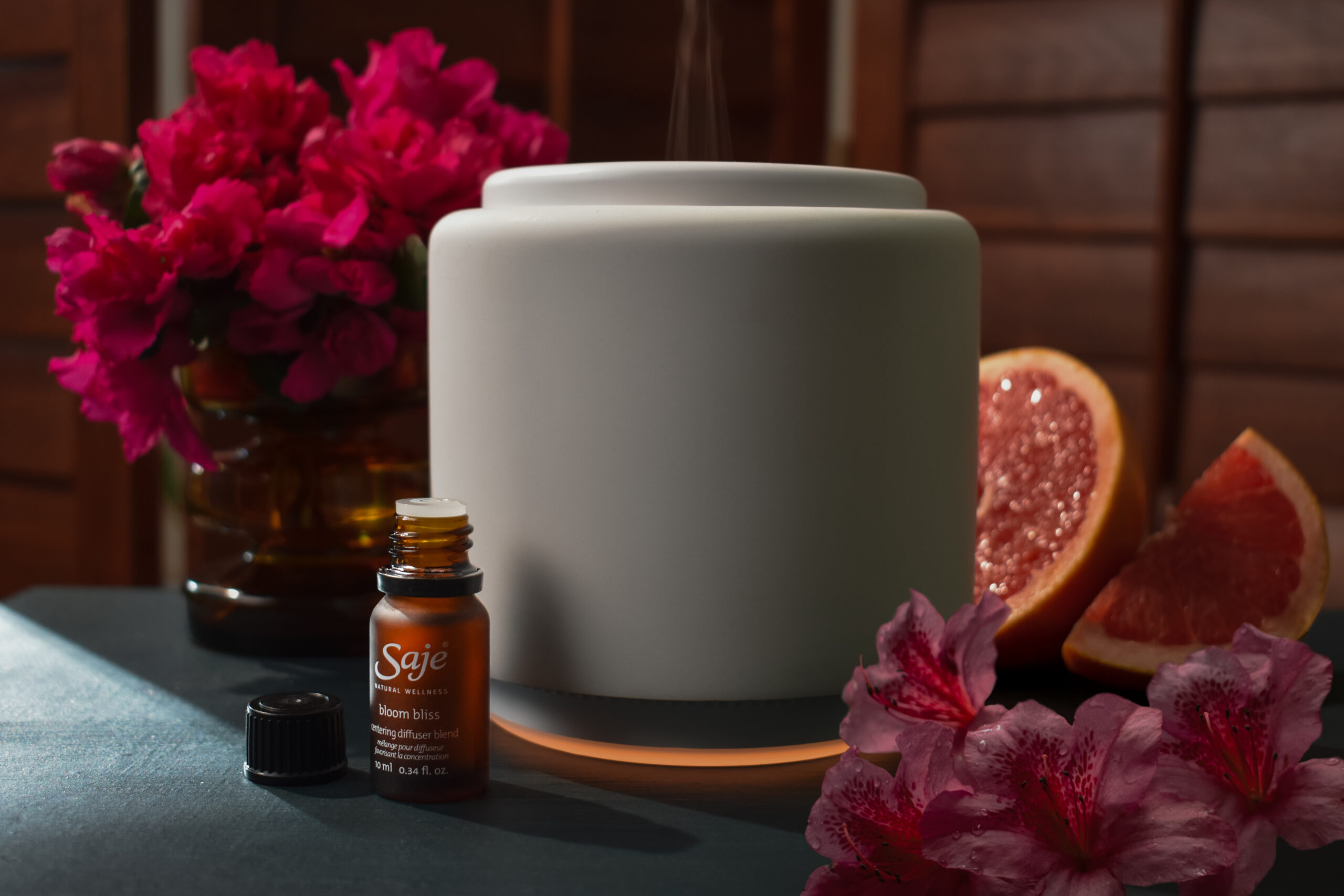Grapefruit and flowers surround a diffuser and a bottle of essential oil on our May wishlist.