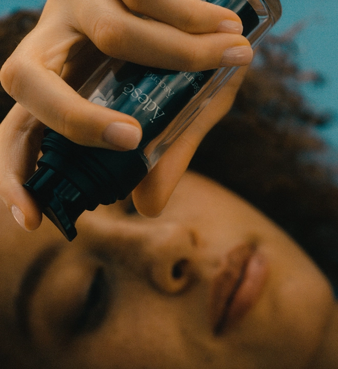 A woman holds a skin care bottle over her face