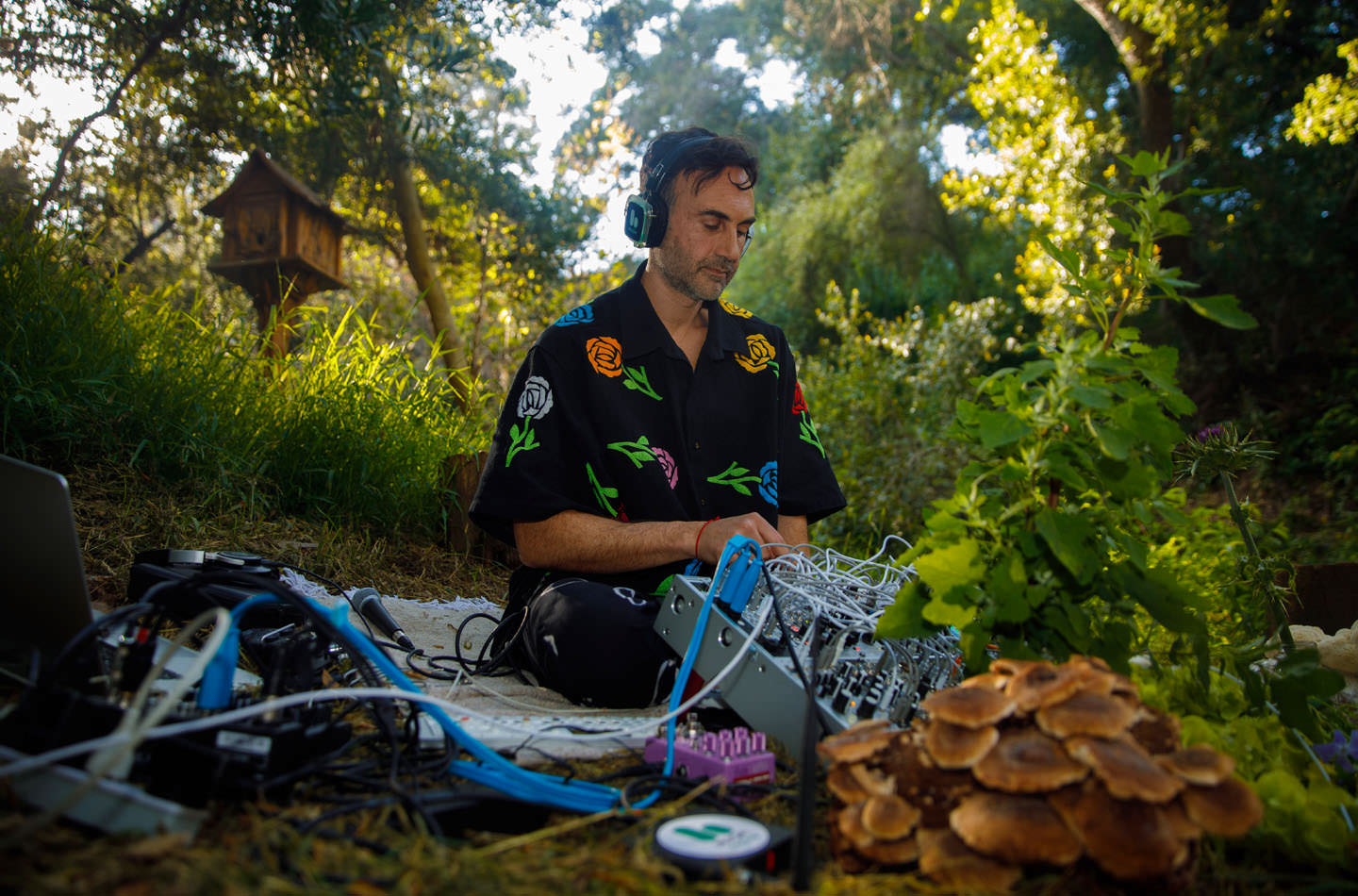 Tarun Nayar, who performs as Modern Biology, sits outdoors wearing headphones and handling musical equipment.