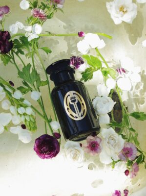 A black glass bottle of Sangre de Fruta bath salt in a tub full of flowers.
