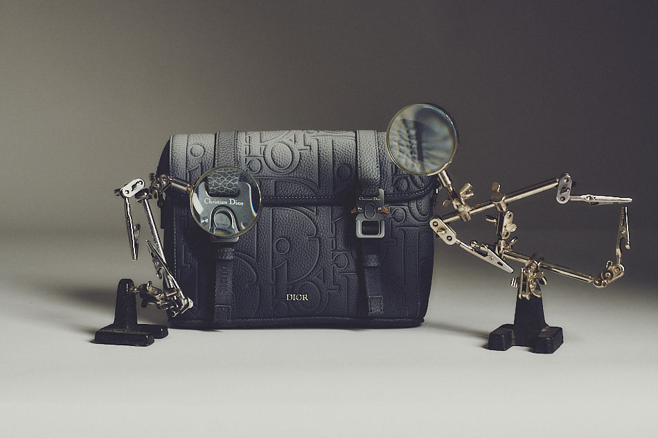 A men's leather bag by Dior, surrounded by two industrial magnifying glasses.
