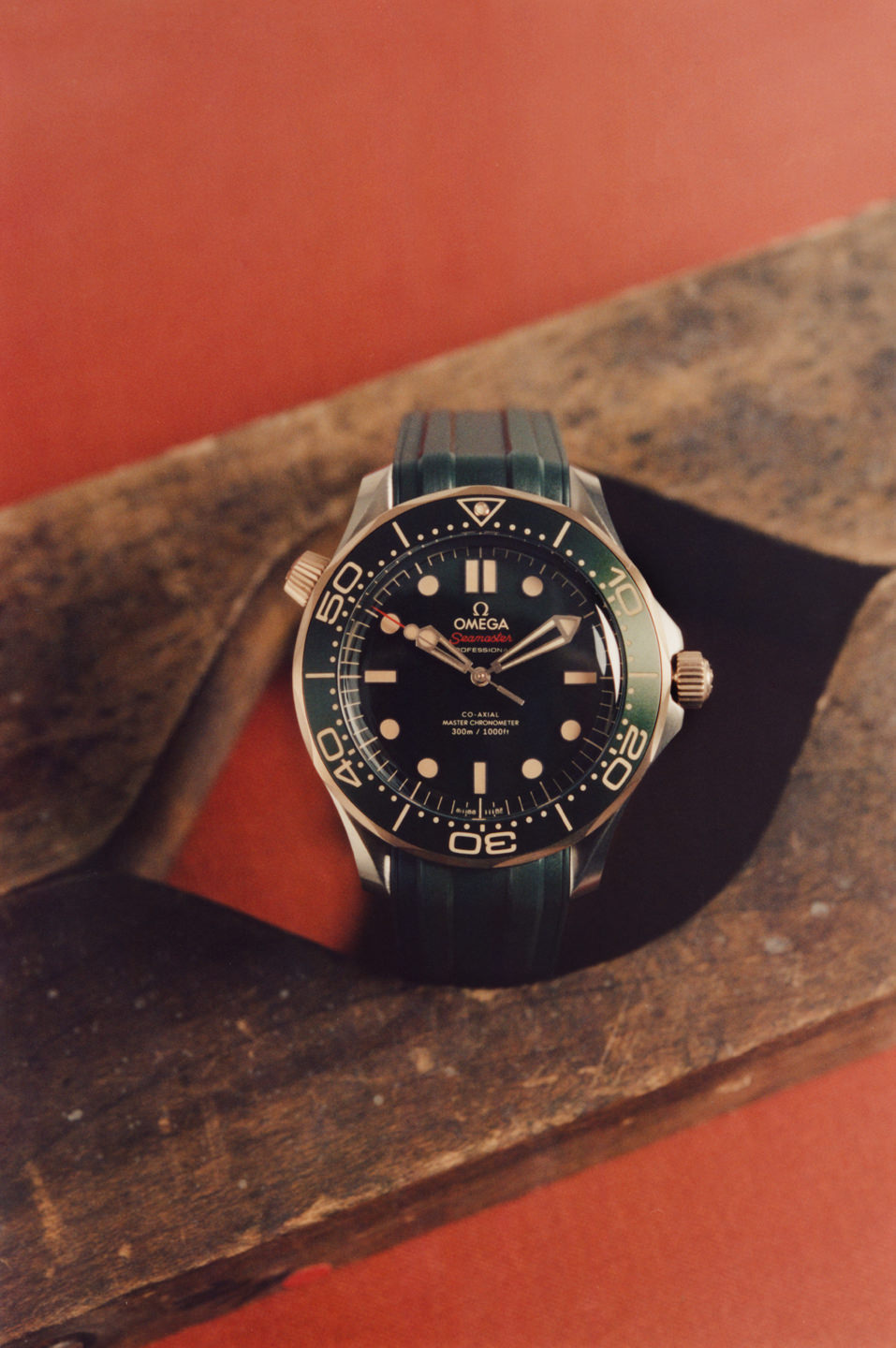 A black, analog wristwatch on a piece of wood against a red background. Men's fashion shoot.