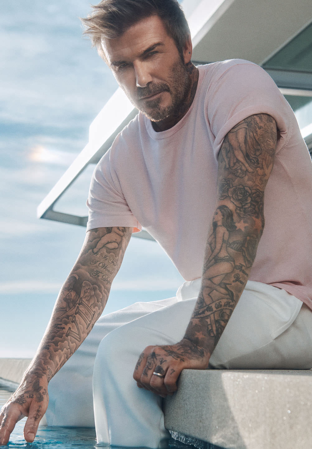 David Beckham wears pink tee and white pants while sitting by a pool as part of our summer ishlist.