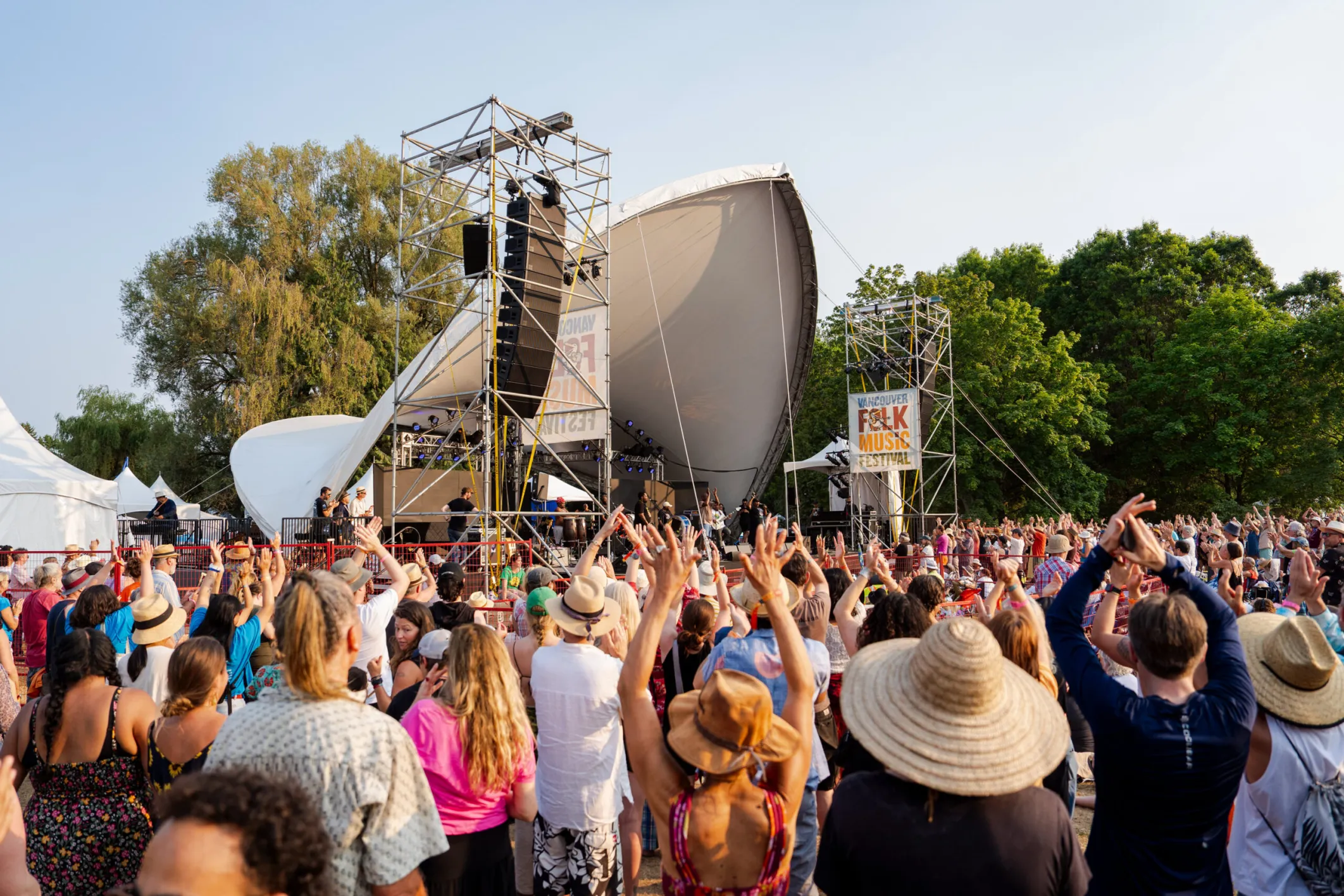 A crowd watched a music stage with their hands raised in the air.