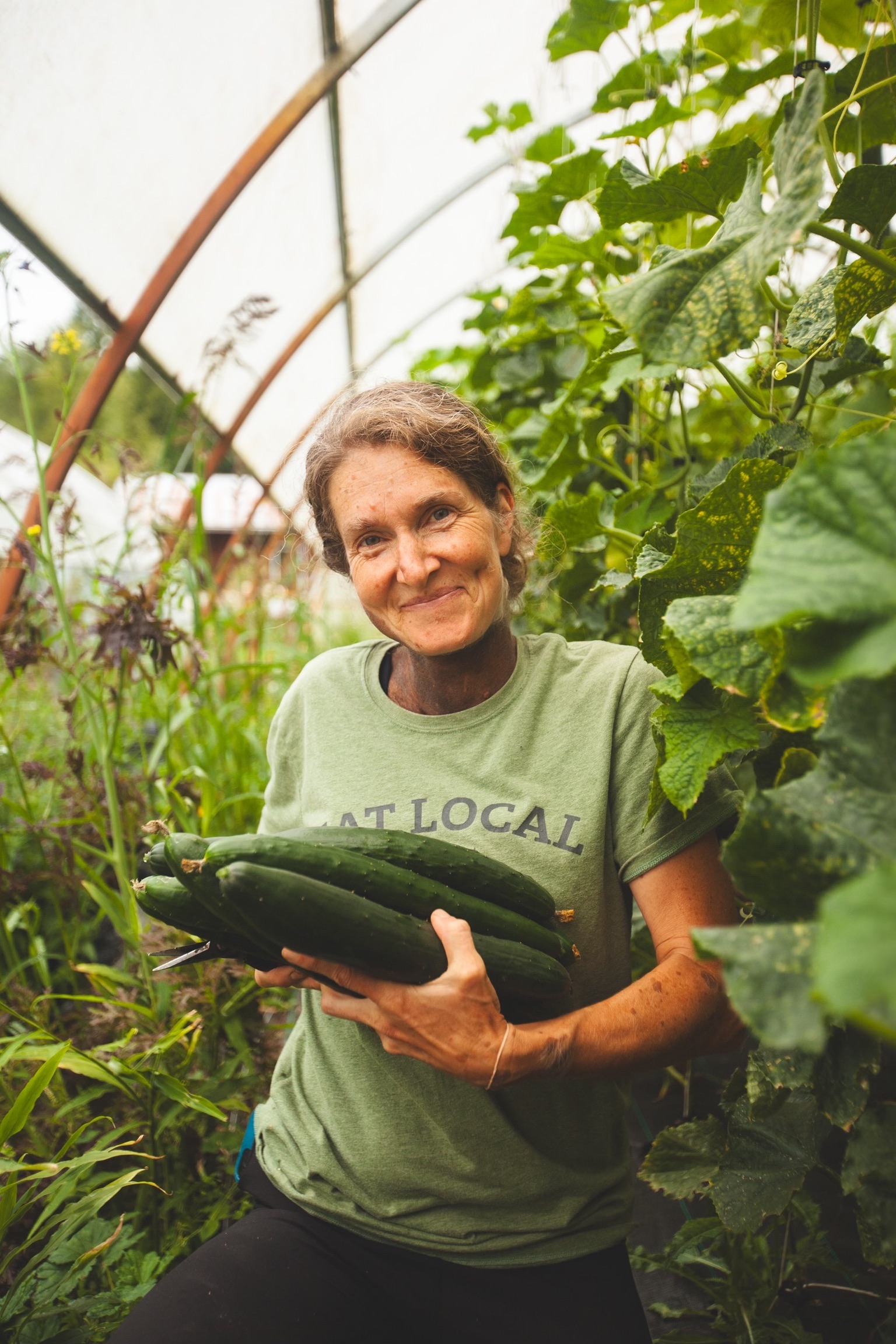 A woman in a greenhouse holds cucumbers.