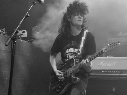 A woman with a guitar plays on stage with Dead Bob in a black and white photo.