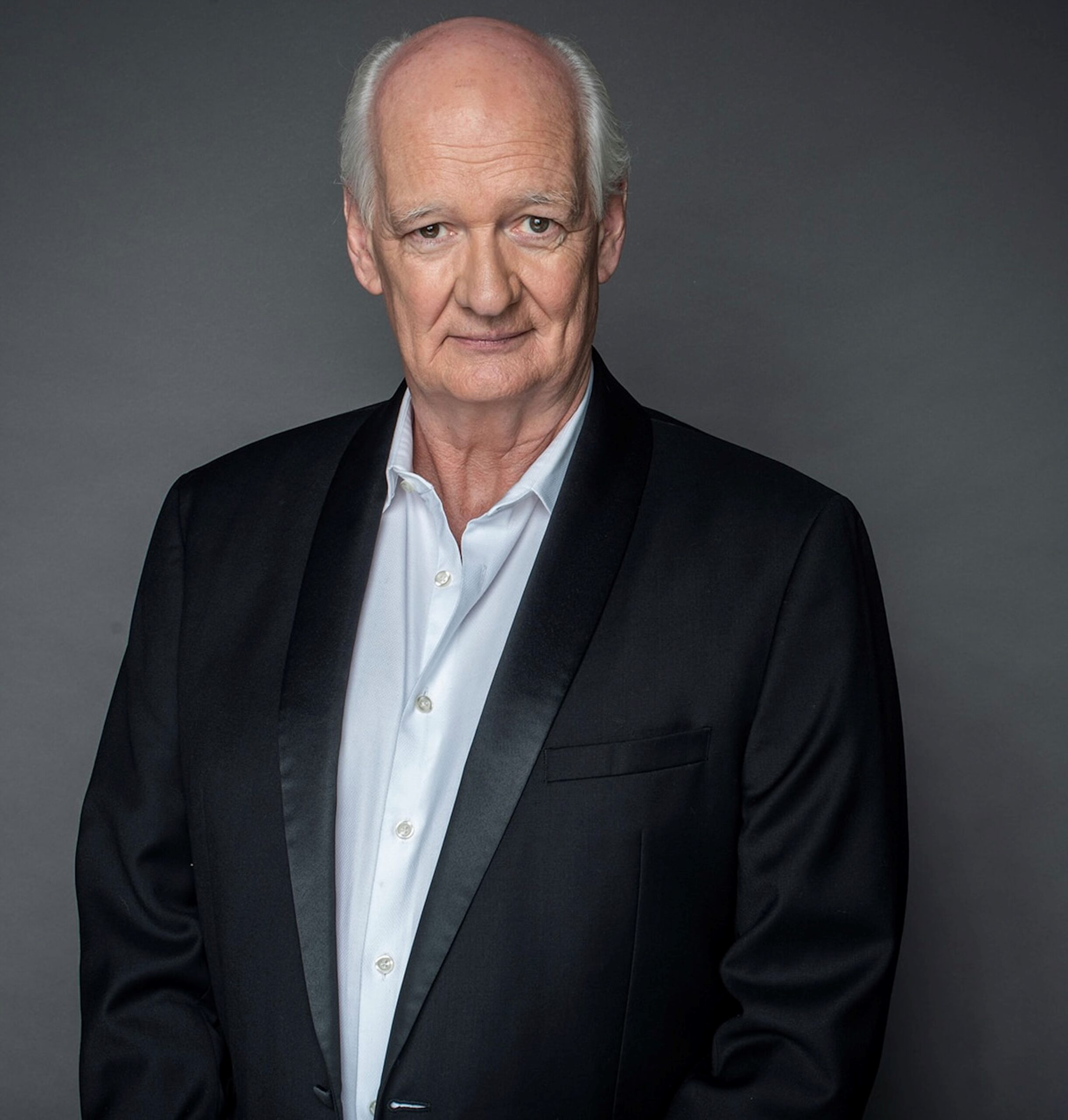 A portrait of Colin Mochrie in a dark suit.
