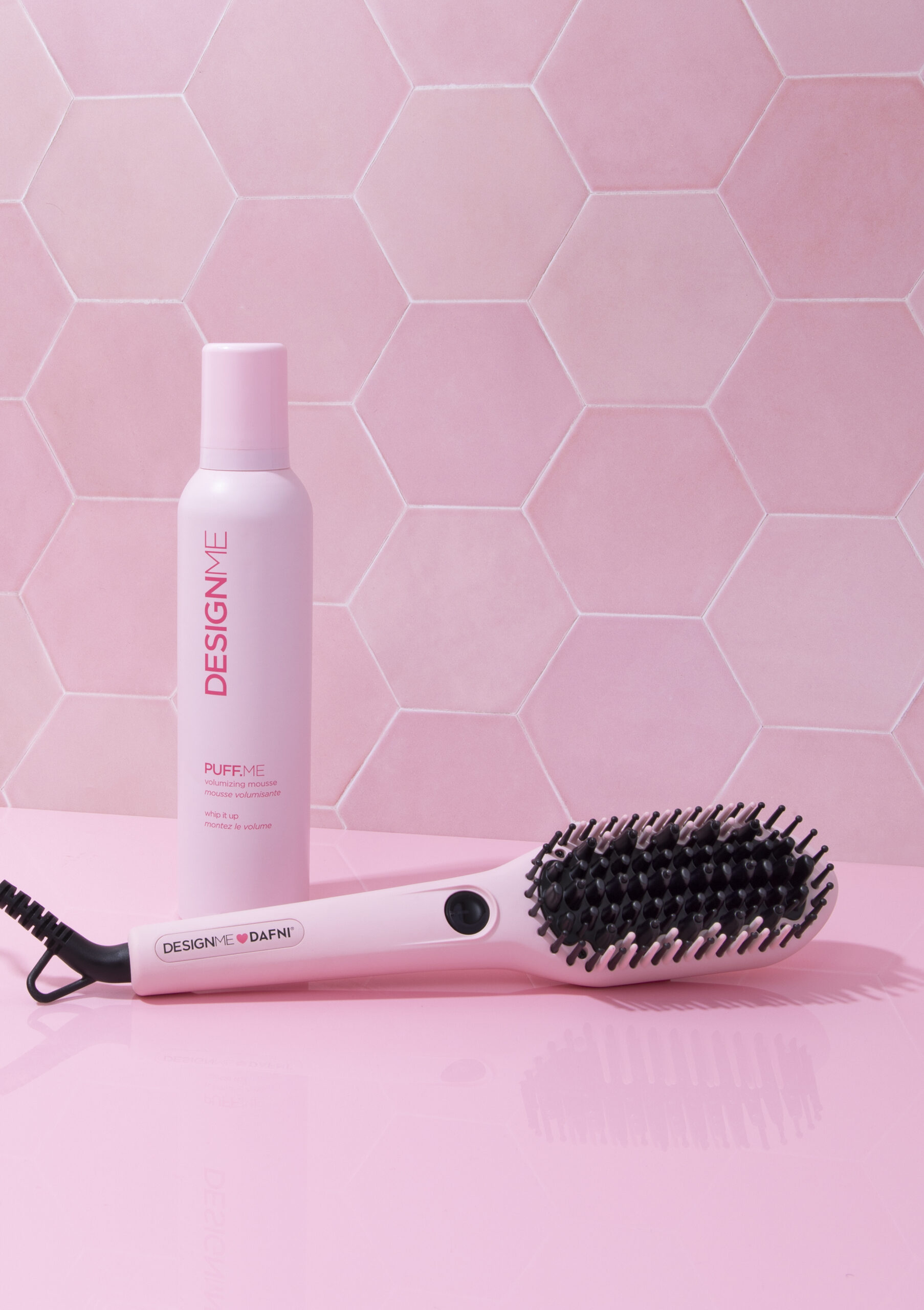A pink electric hairbrush by DesignMe in front of a pink bottle of mousse.