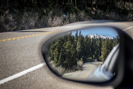 A sideview mirror looking out at highway and forest.