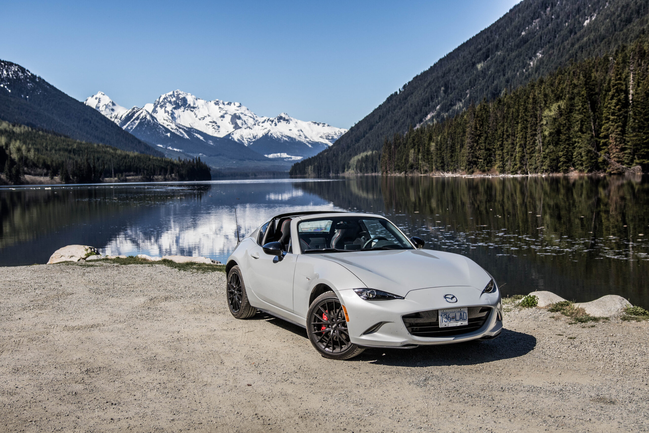 A grey Mazda Miata parked in front of a lake.