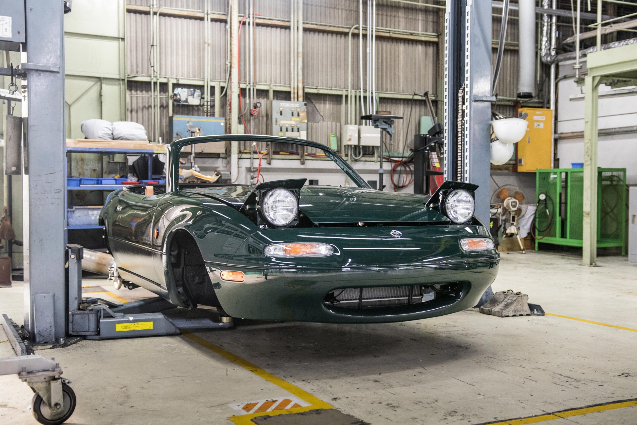 A green Mazda Miata being restored in a garage.