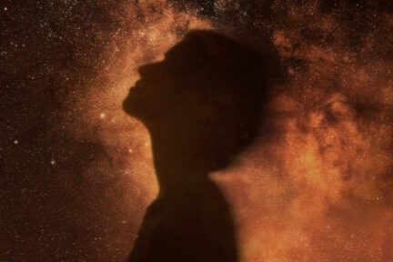 A silhouette gazing up, surrounded by the night sky.