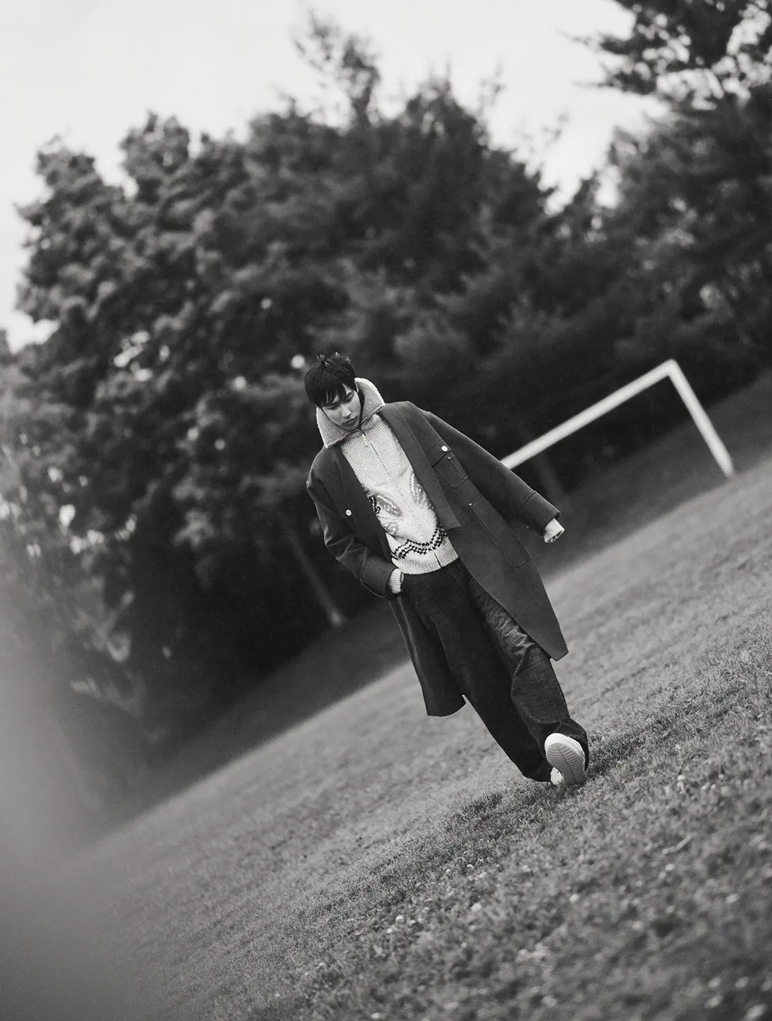 A black and white photo of a man walking through a sports field.