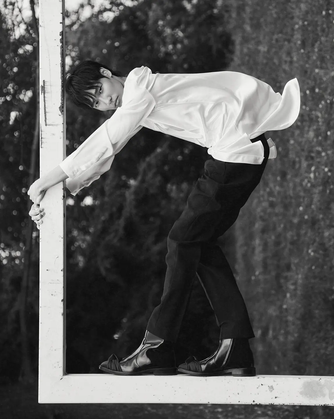 A black and white fashion shoot photo of a man in a suit hanging from goal posts.