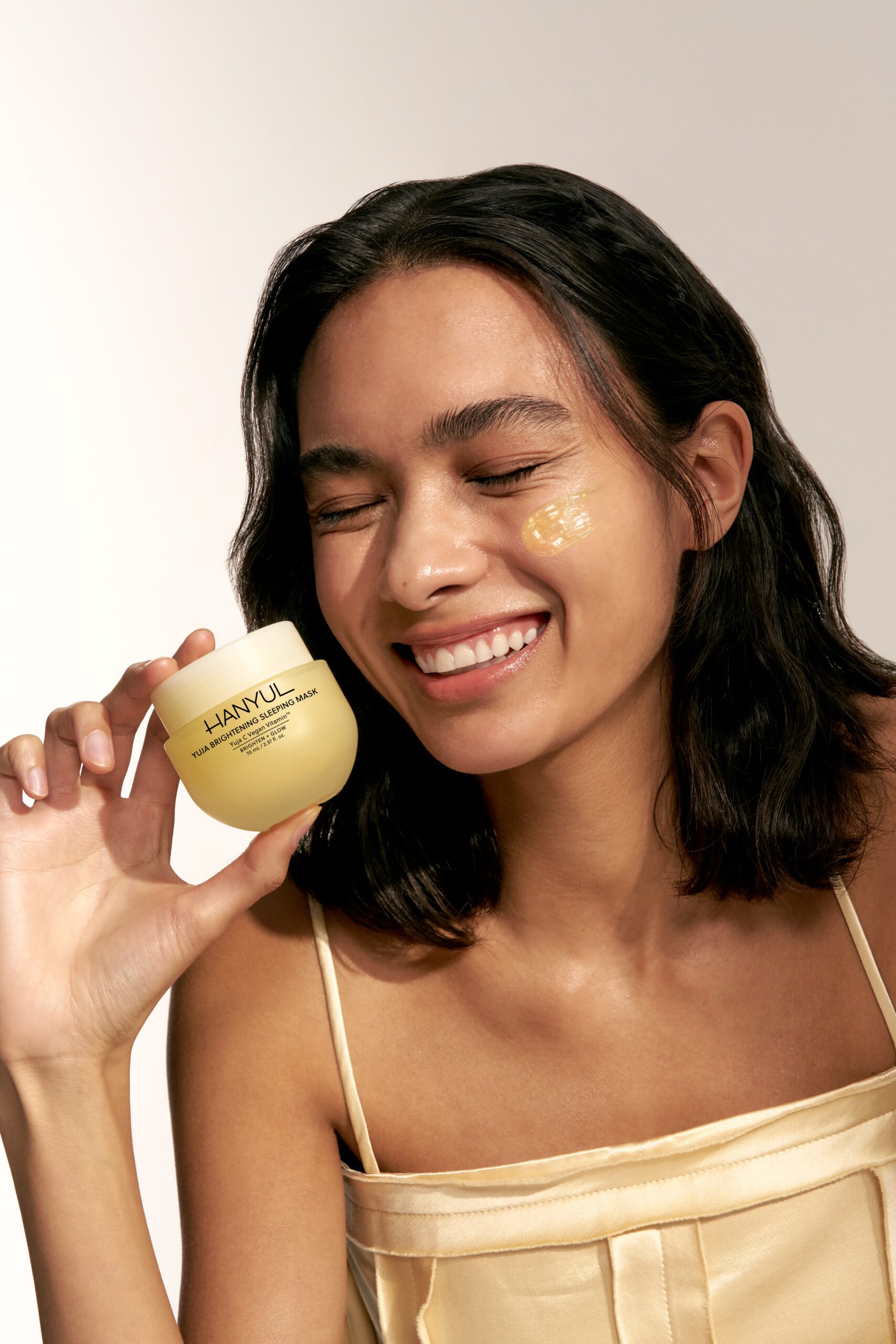 A woman laughs while holding up Hanyul skincare.
