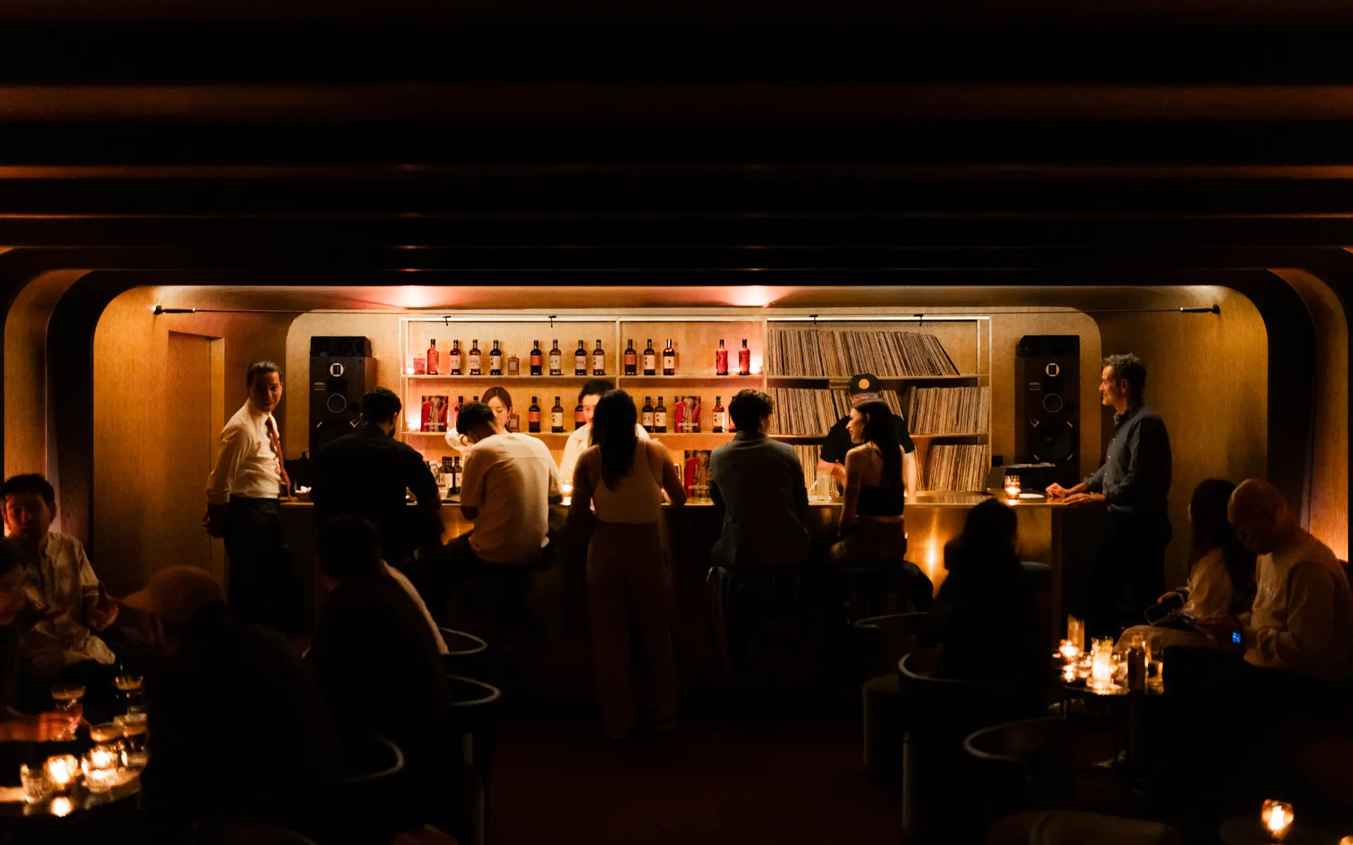 Restaurant patrons shot from behind sit at an illuminated bar.