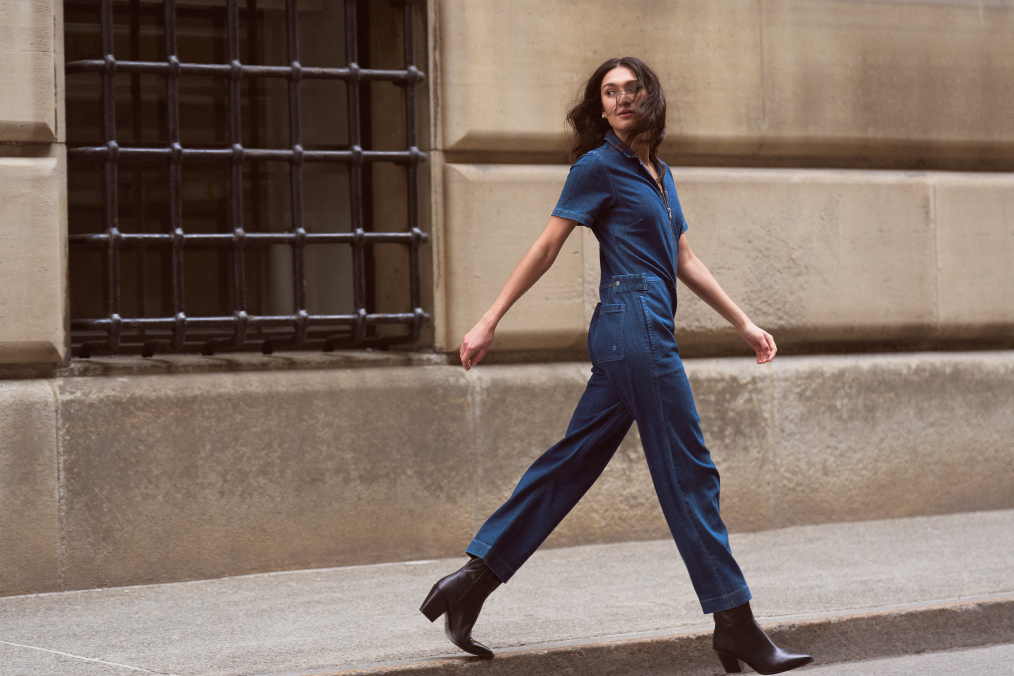 A woman walks down the street wearing a denim jumpsuit from Duer.