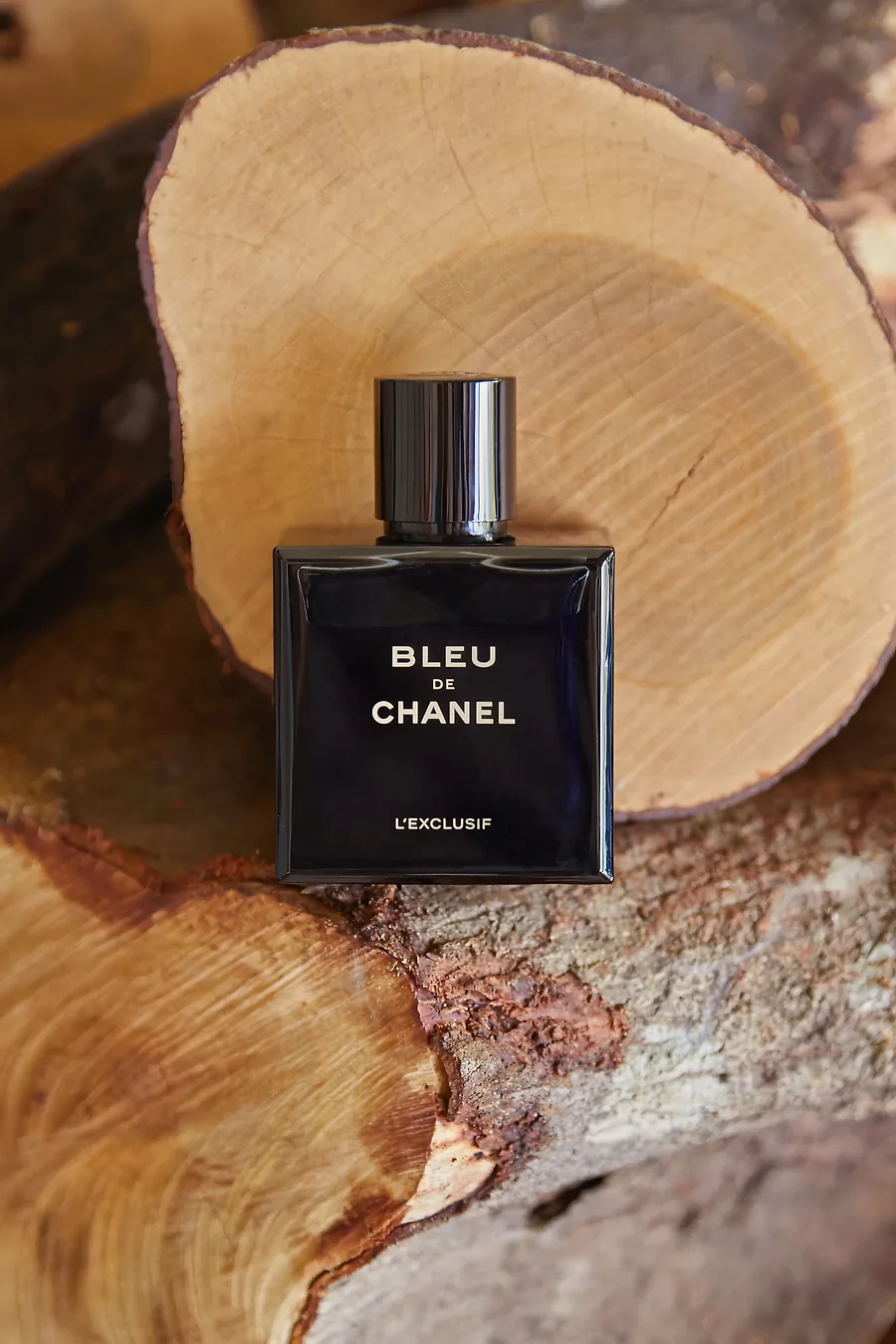 A bottle of Bleu de Chanel perfume in front of a log of wood.