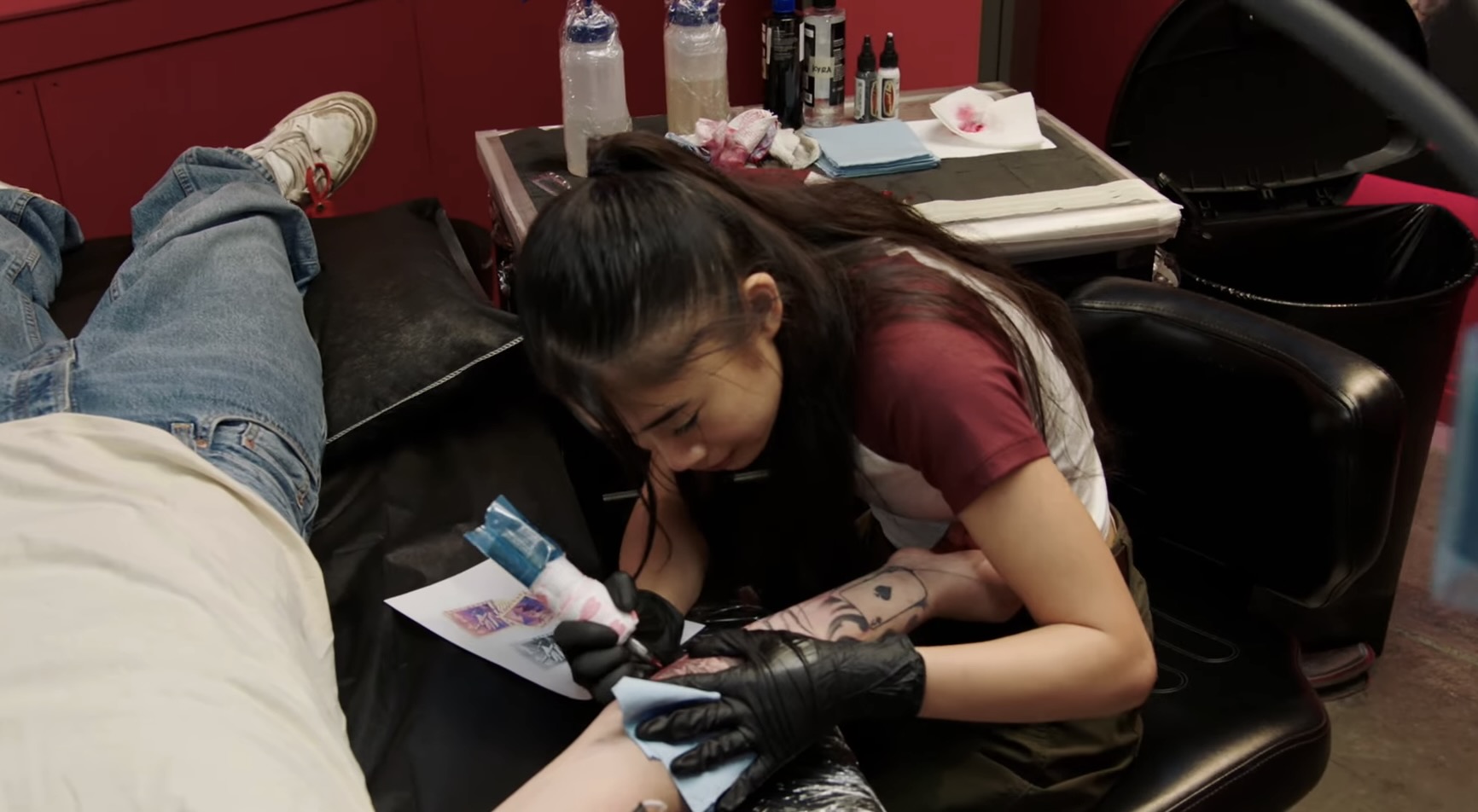 A woman tattoos someone's arm.