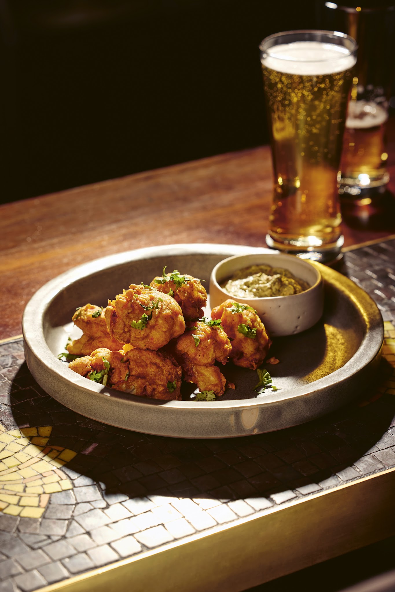 A bowl of fried cauliflower with a pint of beer.