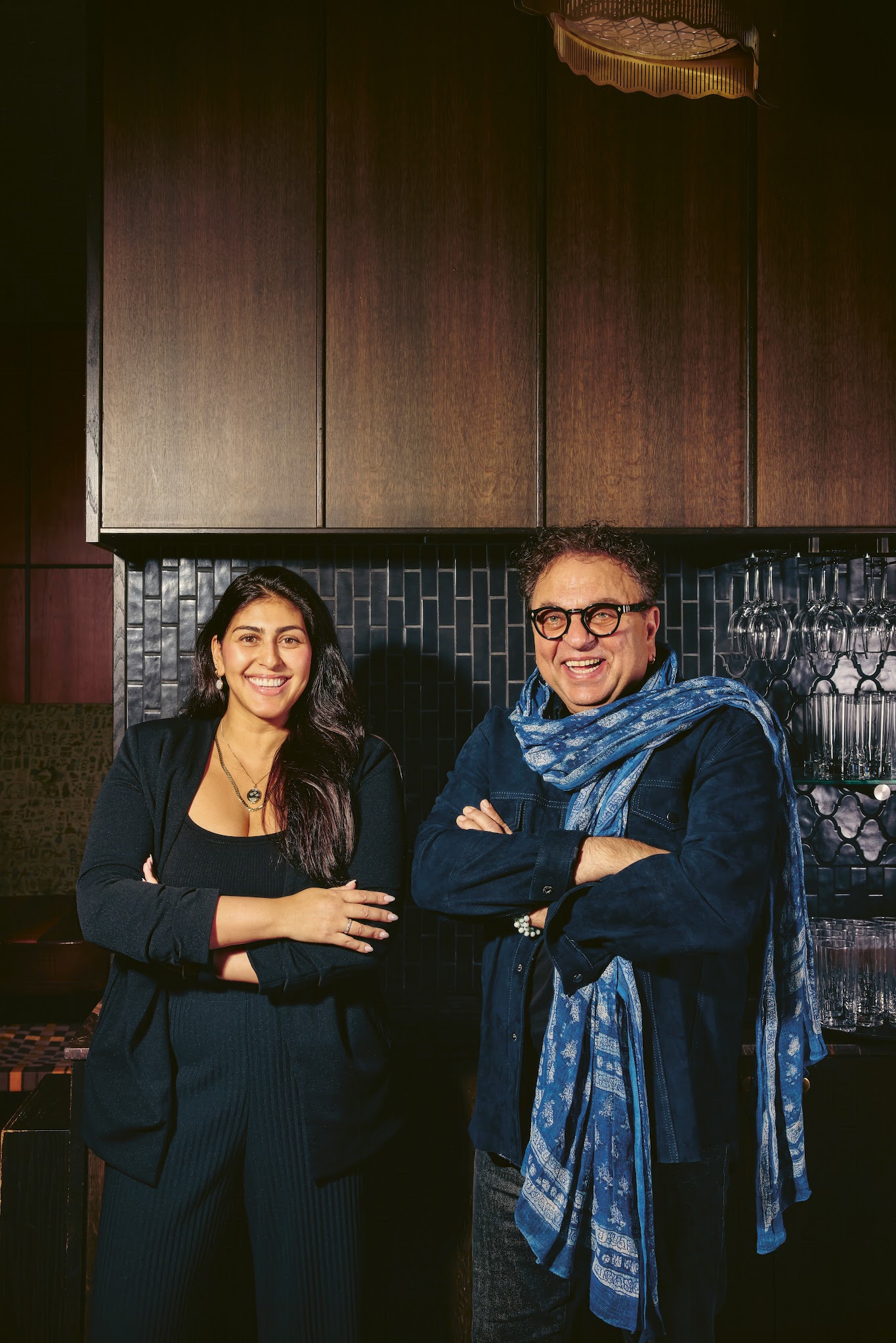A couple stands side by side in a kitchen, facing the camera.