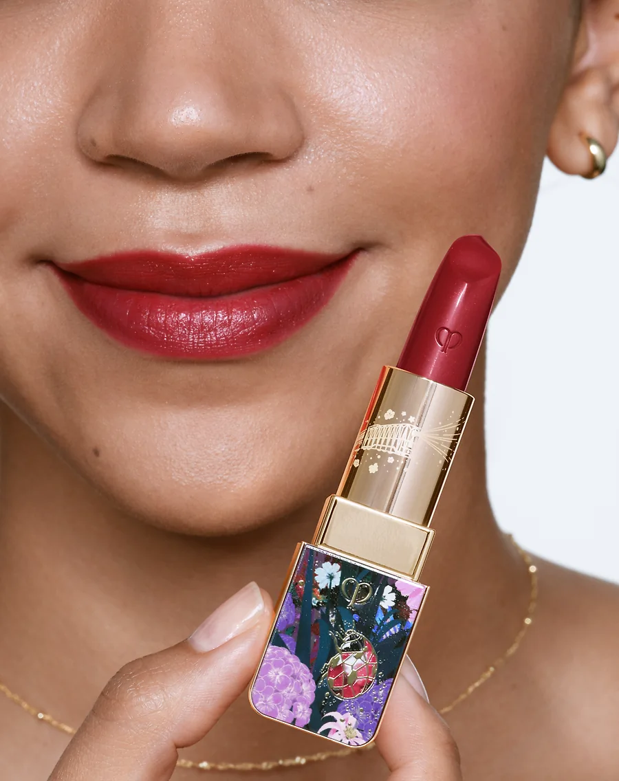 A woman holds red lipstick to her face.