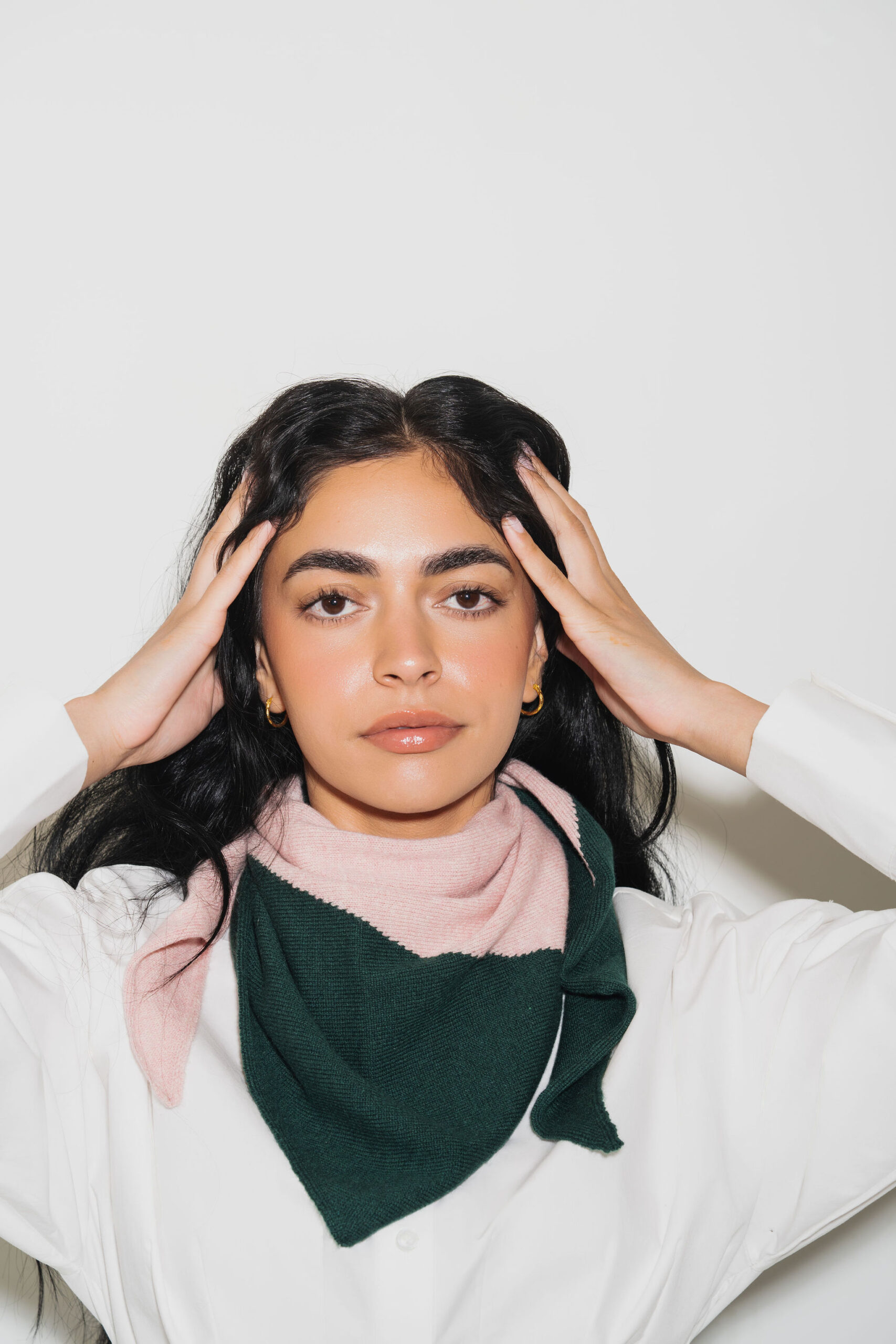 A woman holds her hands up to her temples, wearing a green and pink kerchief.