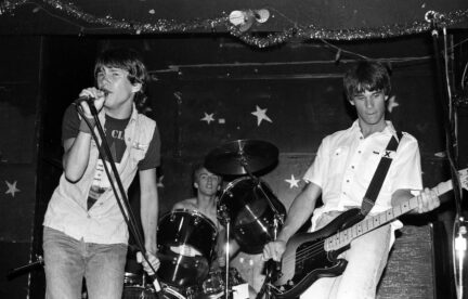 A black and white photo of three musicians (Steve Kravac among them) playing music on stage.