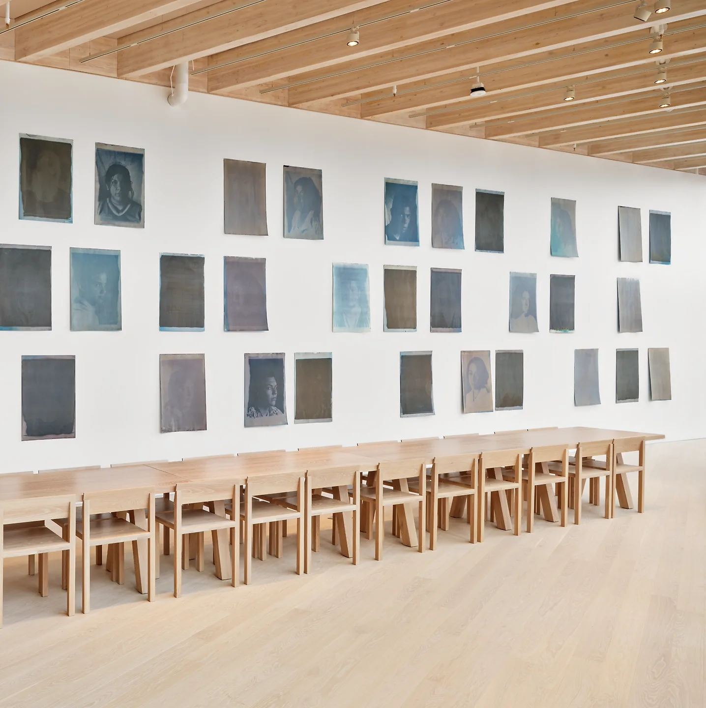 Prints hanging on a wall in front of a long wooden table and chairs.
