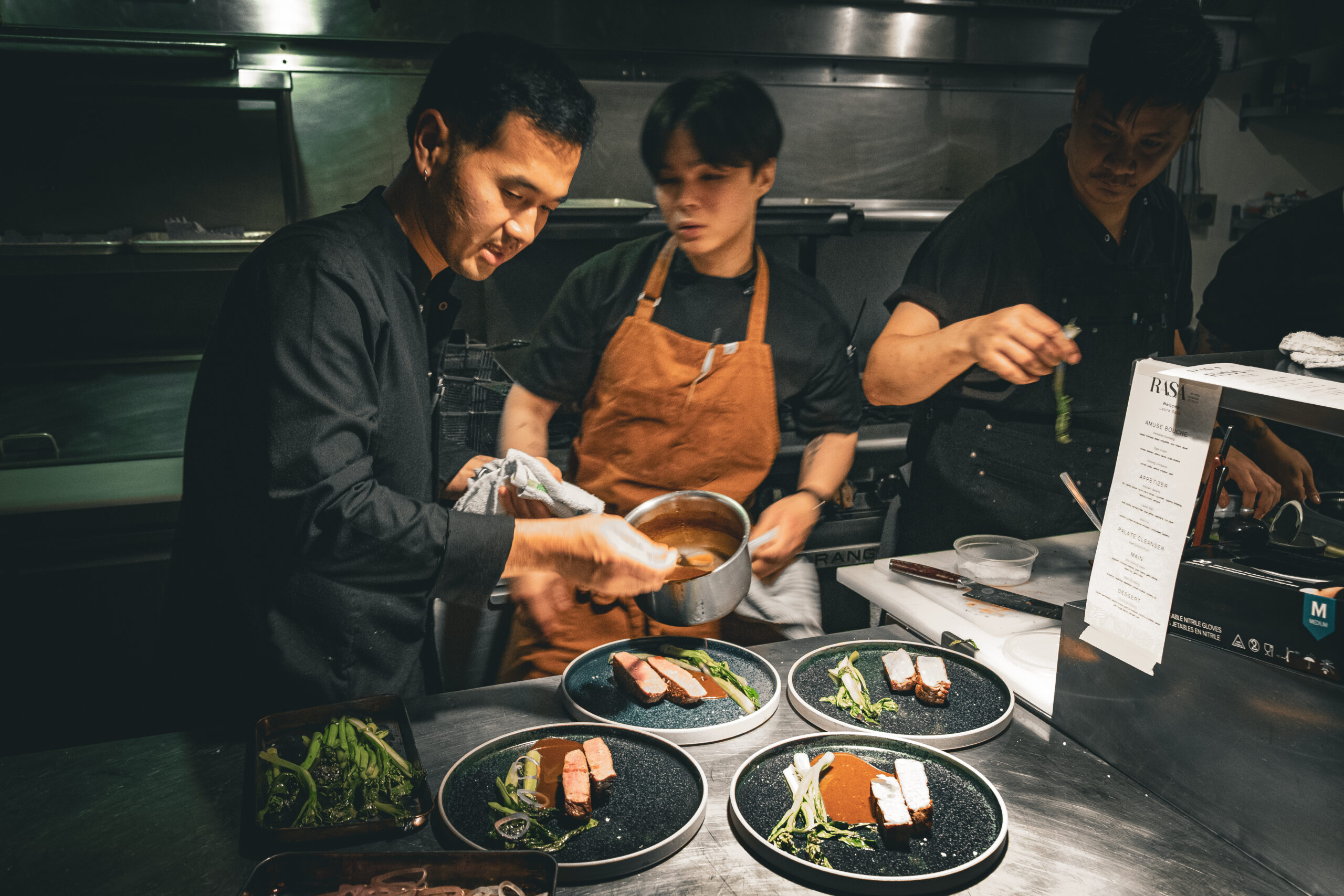 A chef and sous-chefs plate food in a kitchen.