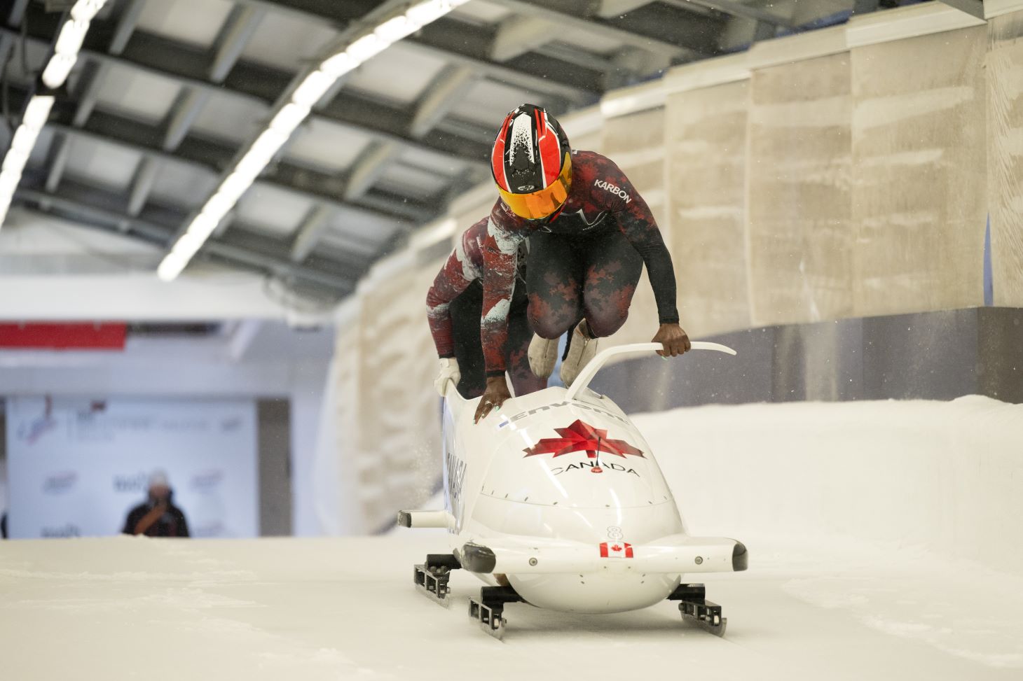 A woman in a Canadian Olympic uniform jumps into a bobsleigh.