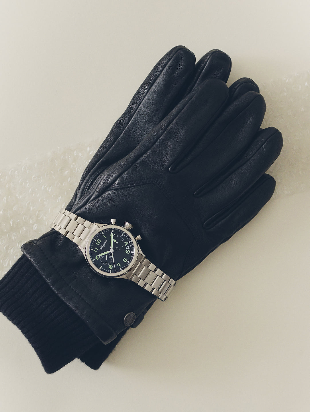 A chronograph watch on a black leather glove.