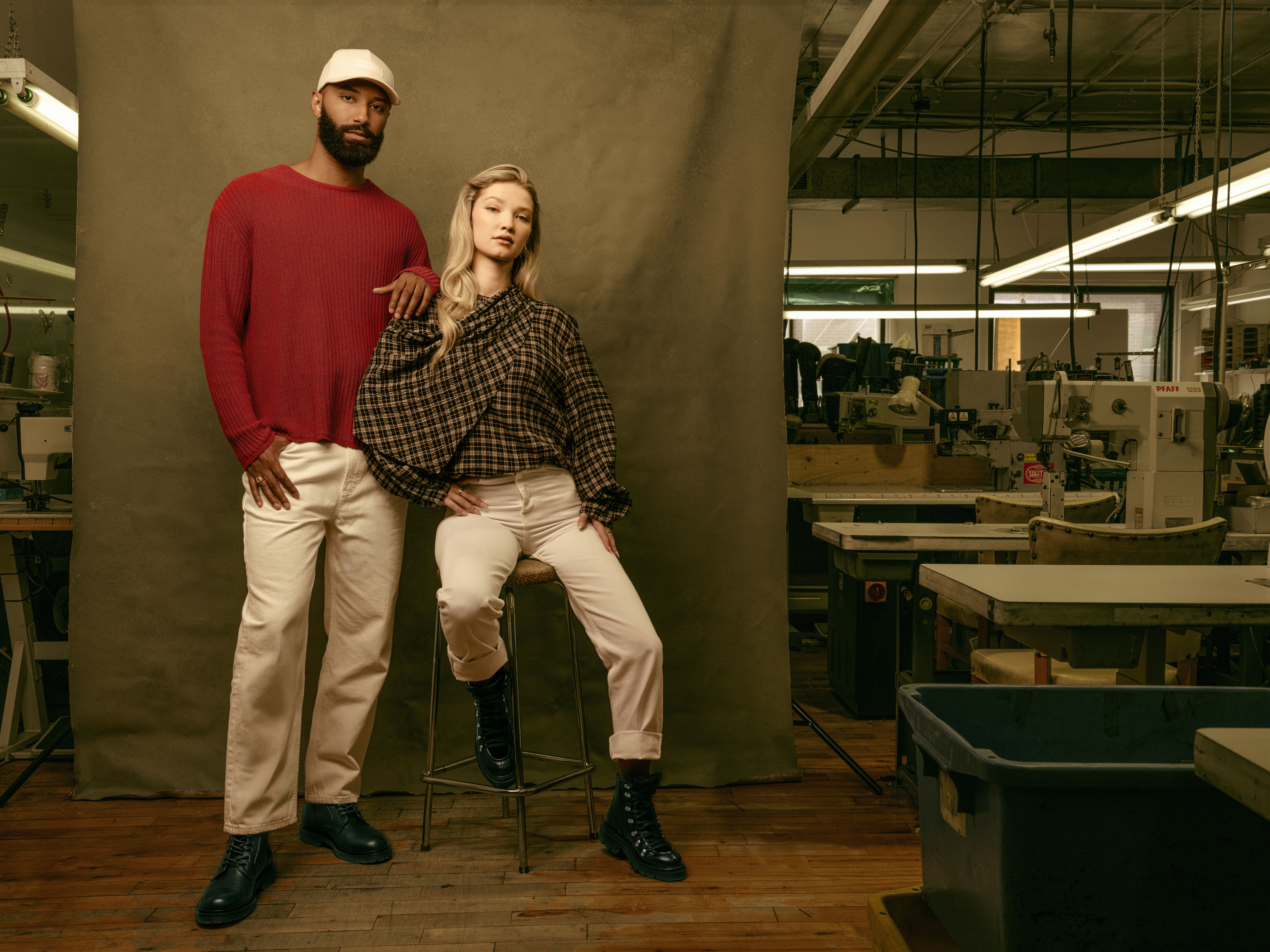 A man and woman model boots in front of a cloth backdrop.