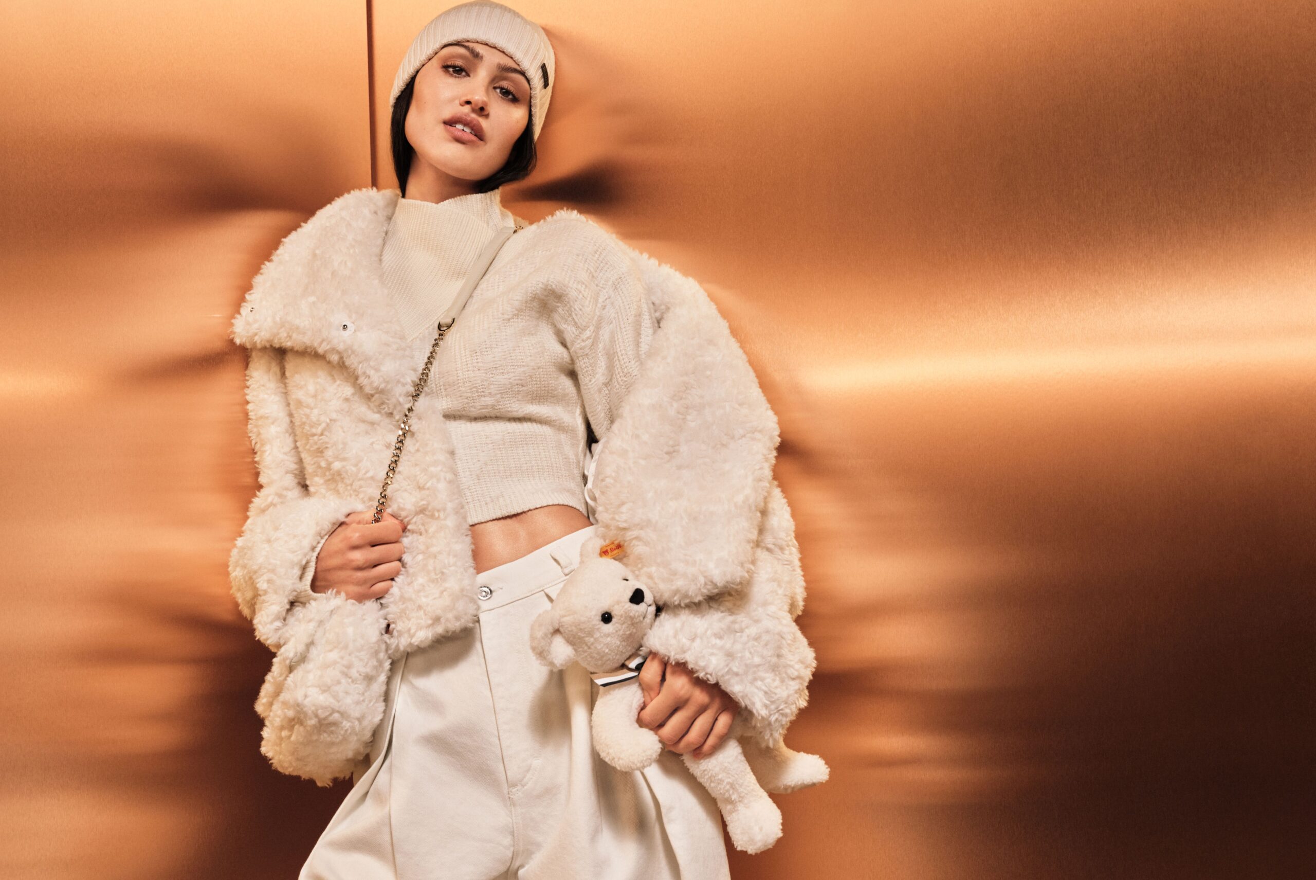 A woman in tan clothes holds a teddy bear.